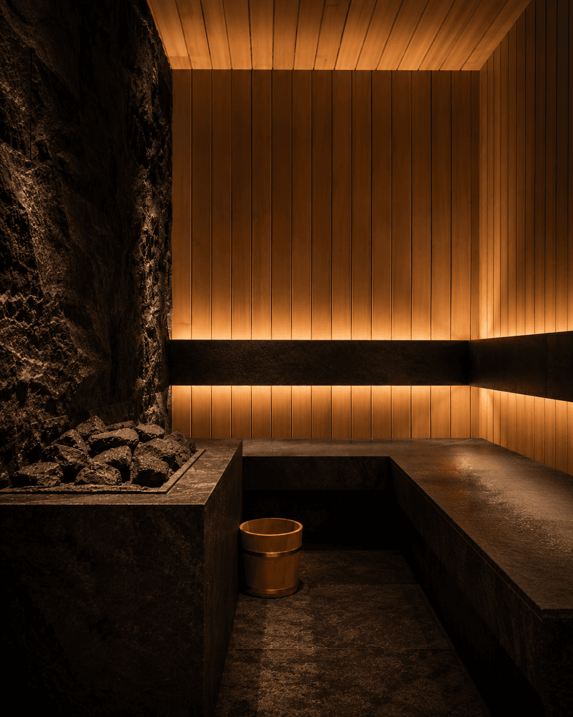 The sauna at Yumori — vertical cypress slats lit from below, a stone bench, a brass bucket beside a tray of volcanic stones